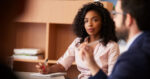 Businesswoman making notes sitting at table meeting with colleagues in modern office