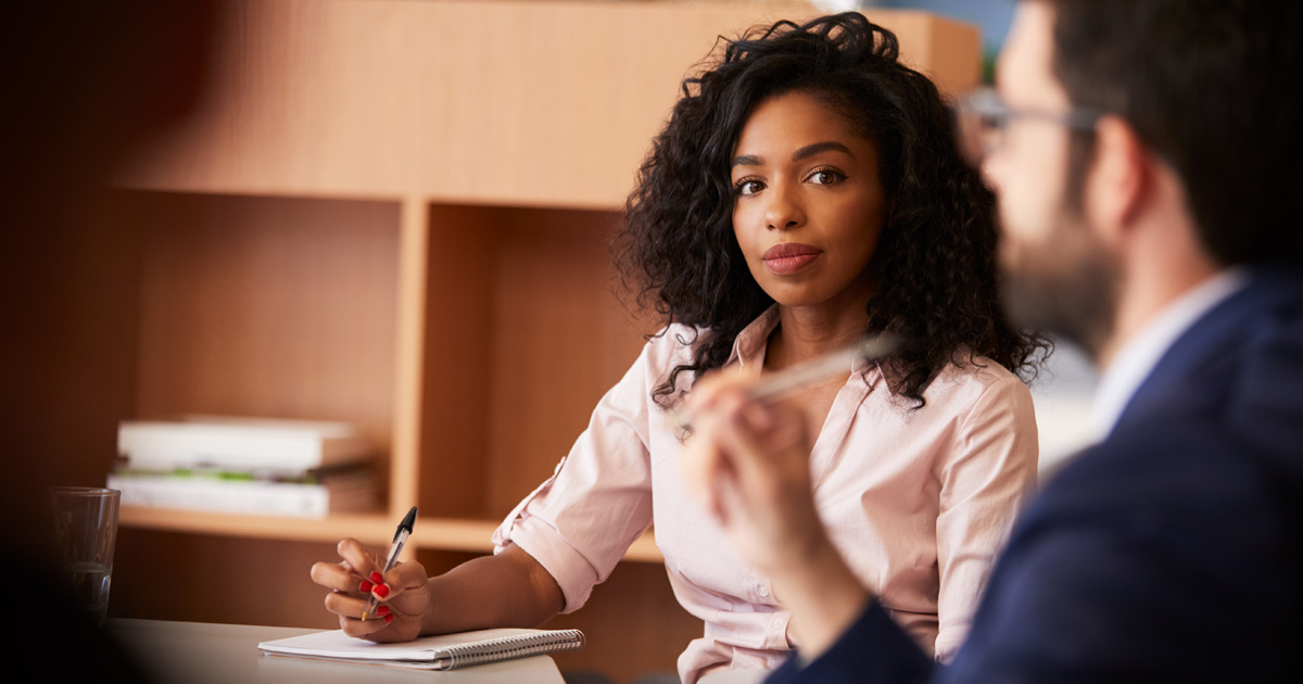 Businesswoman making notes sitting at table meeting with colleagues in modern office
