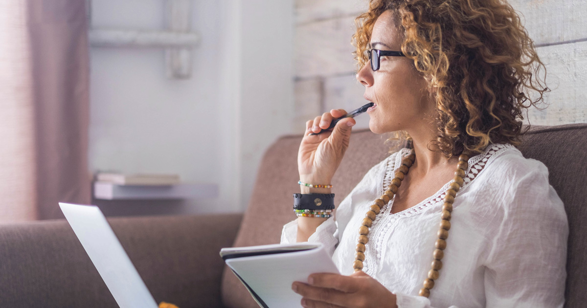 Beautiful woman think and write notes on paper working on a laptop freedom from office at home