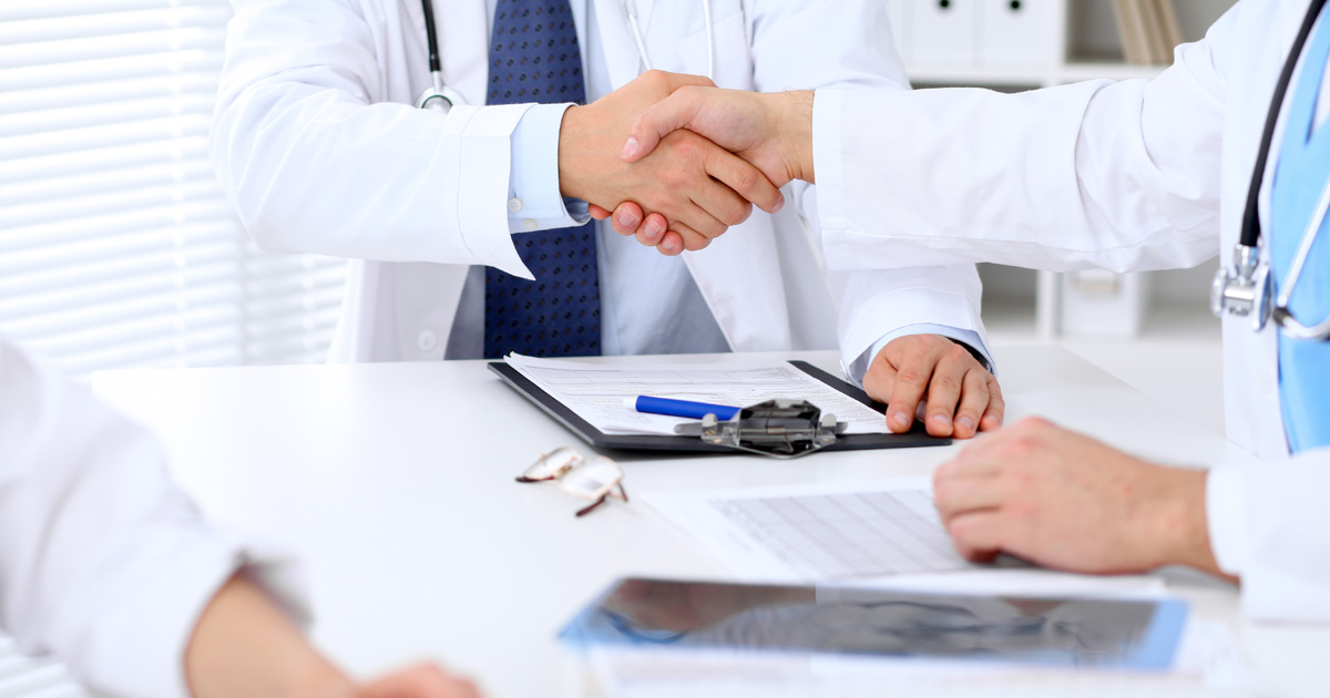 Two doctors shaking hands to each other sitting at the table in hospital office