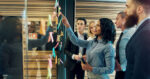 Creative group of business people brainstorming putting sticky notes on glass wall in office