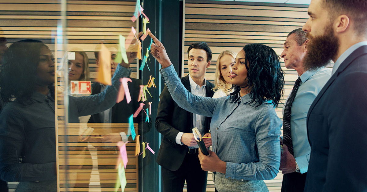Creative group of business people brainstorming putting sticky notes on glass wall in office