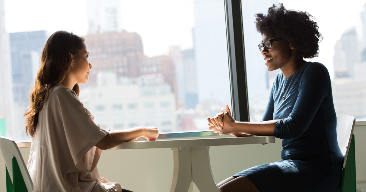 Two women sitting on chairs beside window