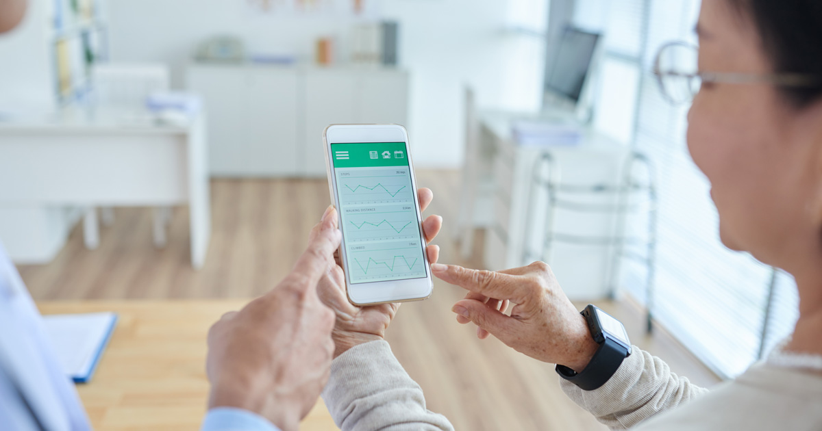 Over shoulder view of middle-aged physician showing his female patient how to use healthcare mobile app