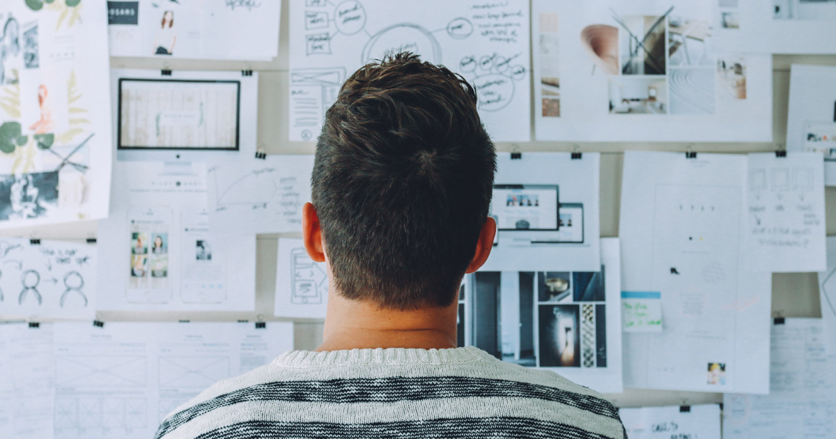 Man wearing black and white stripe shirt looking at white printer papers on the wall