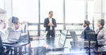 Successful team leader and business owner leading informal in-house business meeting. Businessman working on laptop in foreground