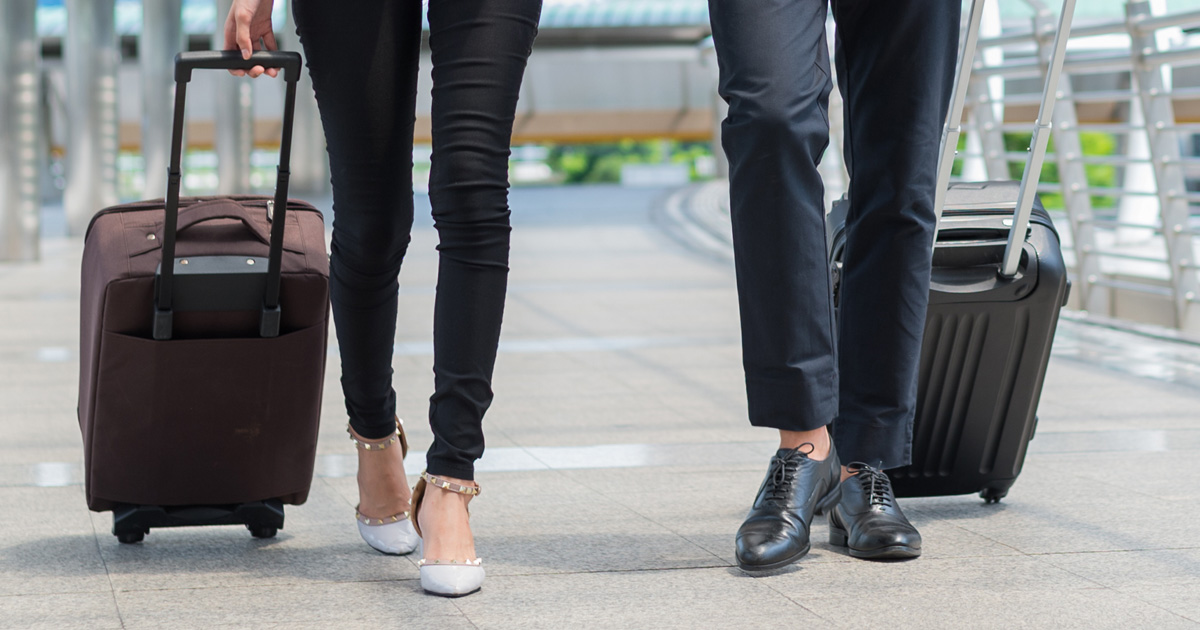 Business man and business woman wear black suit walk together with luggage on the public street
