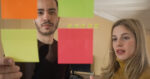 Two young entrepreneurs are brainstorming ideas on sticky notes on the glass wall