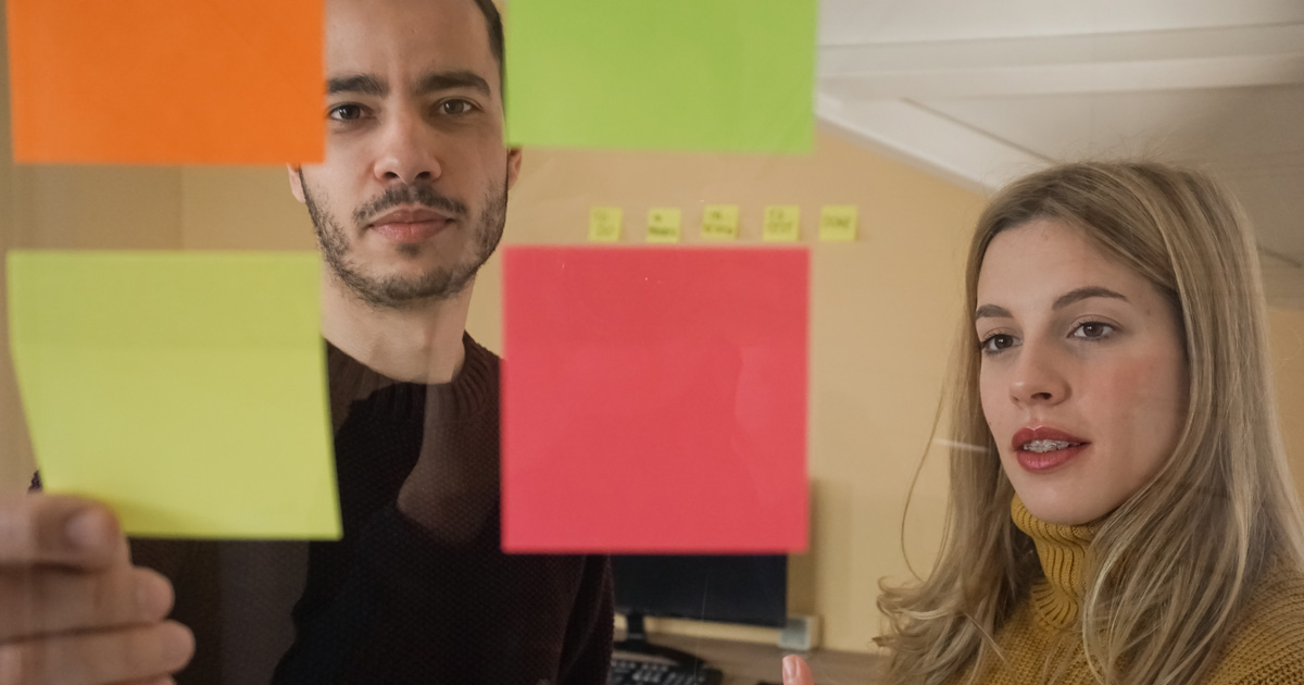 Two young entrepreneurs are brainstorming ideas on sticky notes on the glass wall
