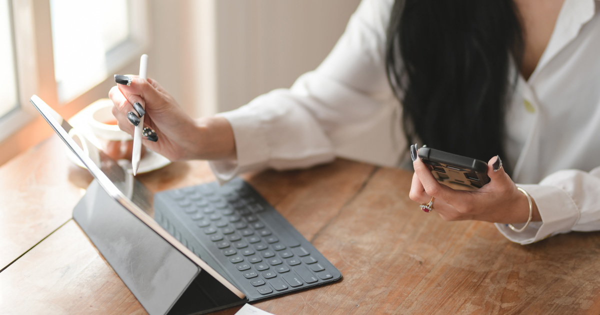 Person in white long sleeve shirt holding black smartphone while using tablet
