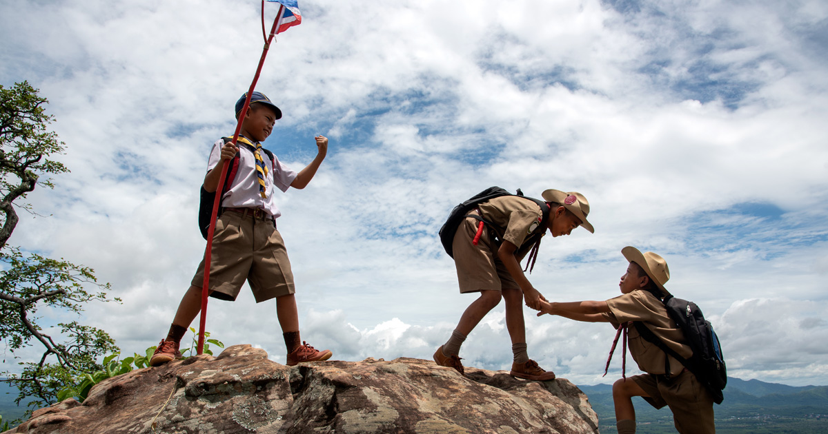 Young American Boy Scouts Help pull up from the cliff