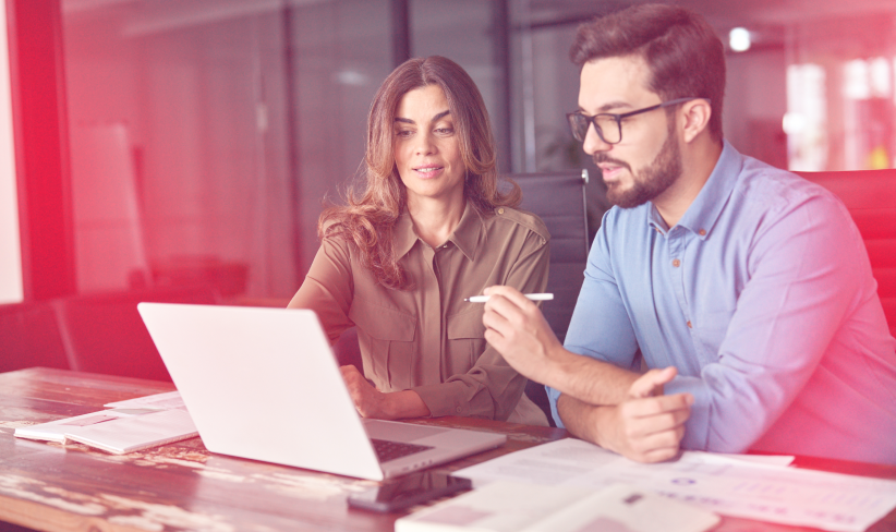 Two business professionals sitting at a desk and looking at a laptop.