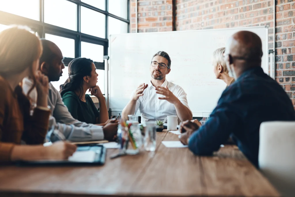 Group of office workers sits at conference table while discussing data governance strategy.