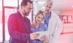 Business consultant speaks with two healthcare professionals while looking at a tablet.