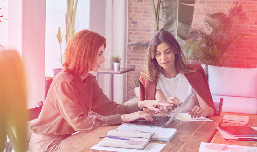 Two business professionals sitting at a table discussing work while looking at papers.