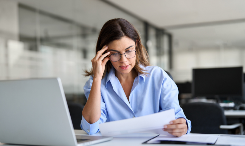 Office worker sitting at desk while looking worriedly at paperwork.