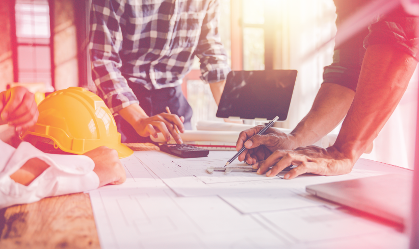 Group of construction workers standing at table looking at papers and using calculator