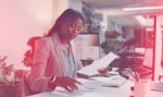 Young professional sits at a desk while looking at papers and Internet of Things data analysis results.