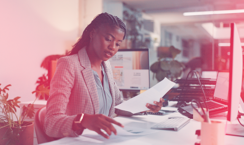 Young professional sits at a desk while looking at papers and Internet of Things data analysis results.