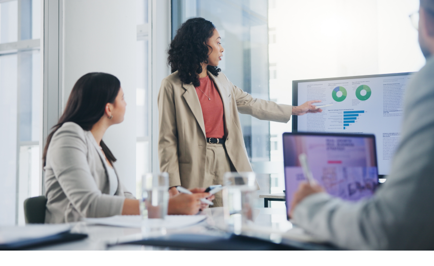 Woman points to screen with graphs while speaking about big data and AI with her coworkers.