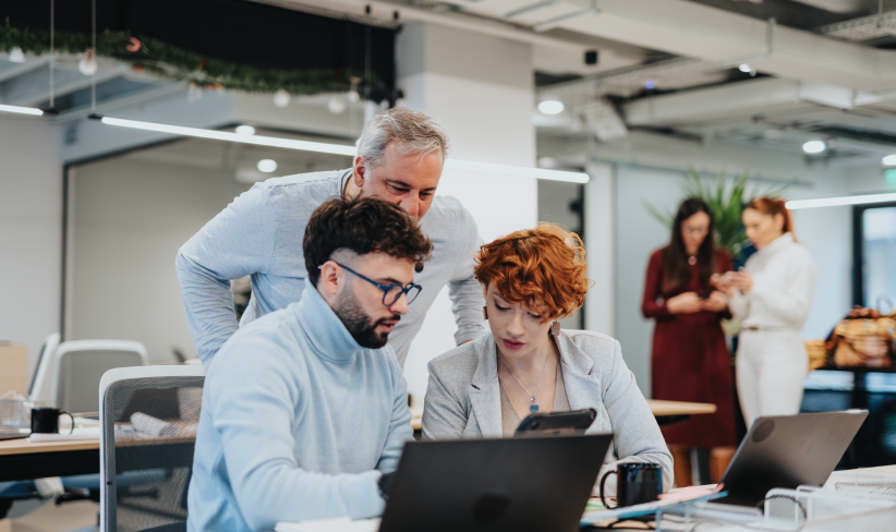 Group of dynamic office workers discuss big data and AI while looking at a laptop.
