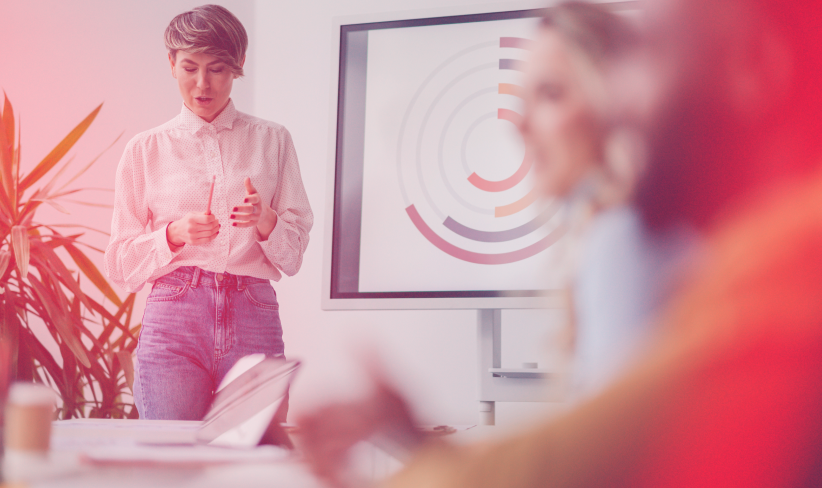 Woman stands in front of large screen with data, presenting to peers