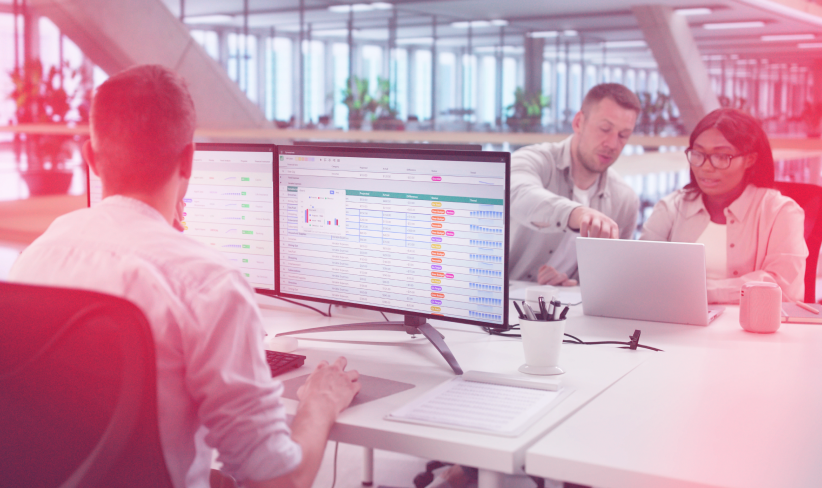 Man looking at spreadsheets on his computer while two coworkers across from him look at laptop