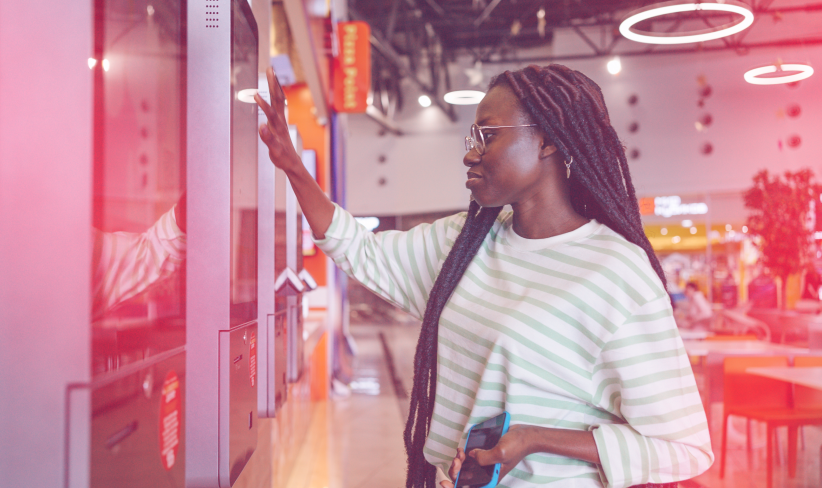 Woman in a quick-service restaurant placing an order at a self-serve kiosk