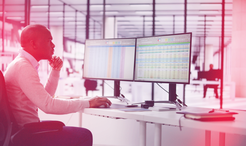 Professional looking at two monitors of data while working in an office