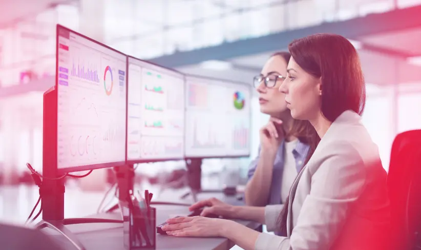 Two professional data analysts looking at multiple computer screens